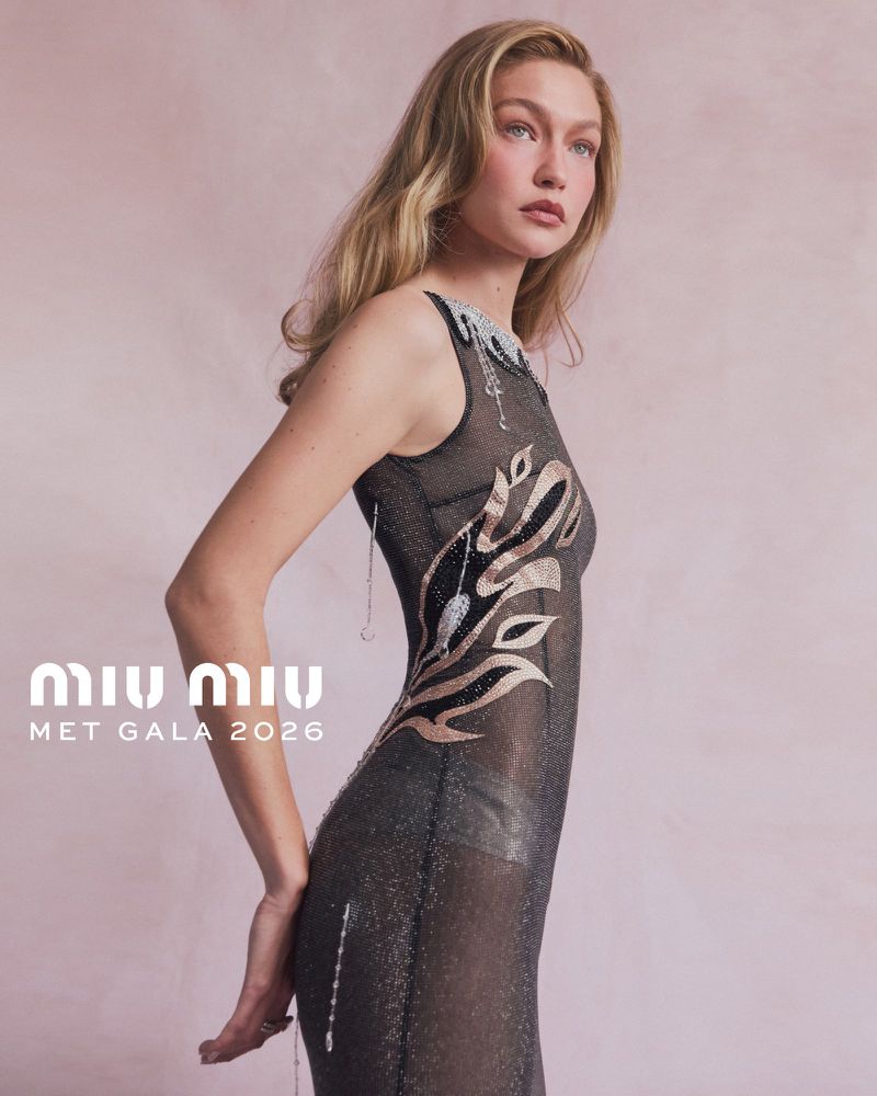 Gigi Hadid posing in a sheer embellished black gown against a soft pink textured studio backdrop for Miu Miu.