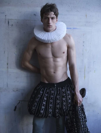 Model Vasko Luyckx shirtless wearing a white pleated Elizabethan ruff collar and Renaissance breeches against a studio wall.
