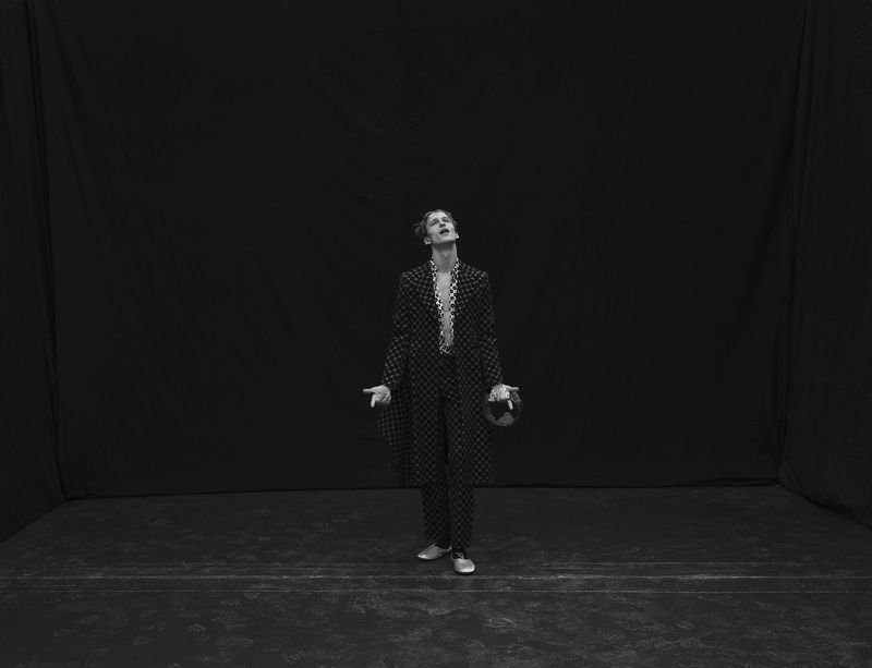 Model Vasko Luyckx in a patterned coat and trousers looking upward against a dark studio background.