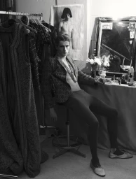 Model Vasko Luyckx seated backstage in a dressing room wearing a patterned jacket and tights for Dapper Dan Magazine.