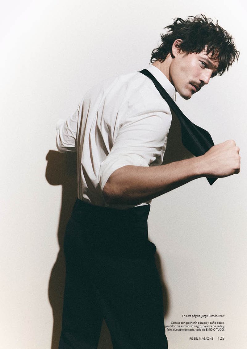 Model Jorge Román wearing a white dress shirt and black trousers with an untied black tie against a white background.