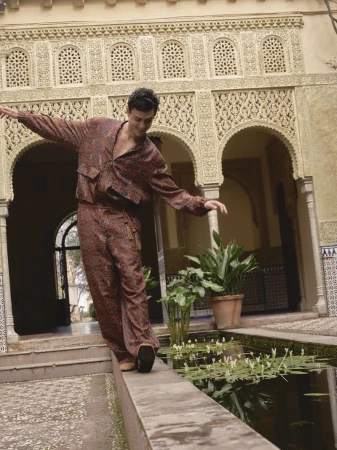 Xavier Serrano balances along a stone pool ledge wearing a patterned brown set in an ornate Moorish courtyard.