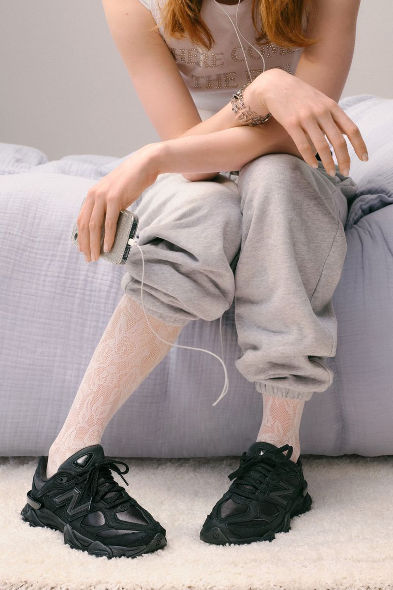 A person sitting on a bed wearing grey sweatpants, black sneakers, and white patterned stockings, holding an mp3 player, listening to headphones.