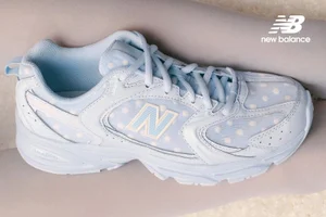 Pale blue New Balance sneaker with white polka dots on mesh panels, displayed horizontally against legs in light tights.