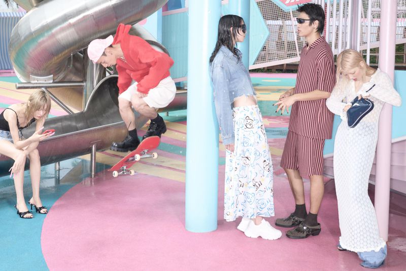 Group of young adults in fashionable clothing on a colourful playground setting with a slide and skateboard.