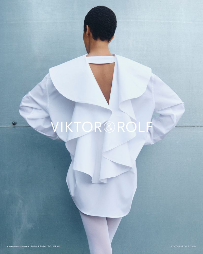 Model seen from the back wearing an oversized white ruffled shirt against a blue wall for Viktor and Rolf SS26 campaign.