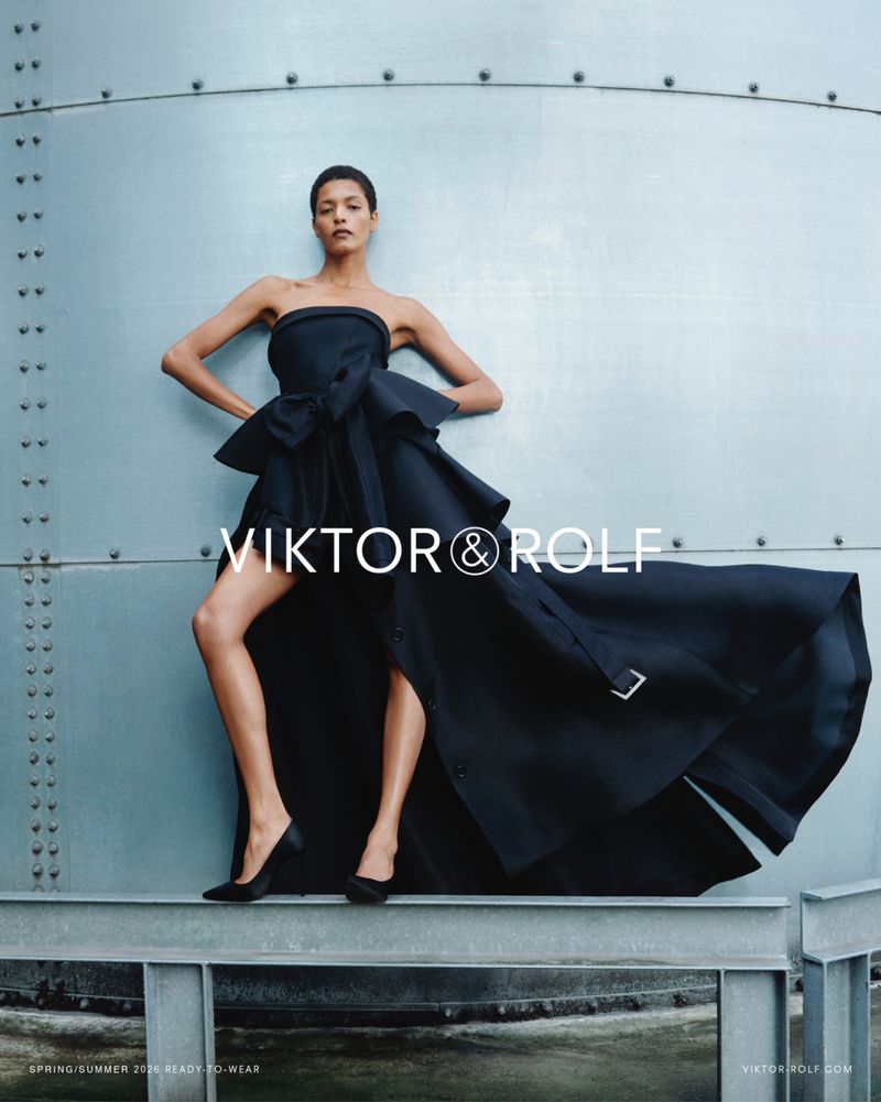 Model Laiza de Moura in a sculptural strapless black high-low gown and heels on an industrial steel beam for Viktor & Rolf.