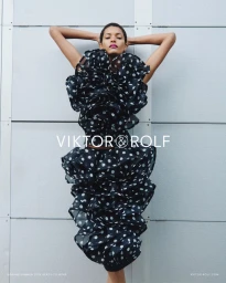 Model Laiza de Moura posing in a voluminous black and white polka dot ruffled dress against a grey panelled wall for Viktor and Rolf.
