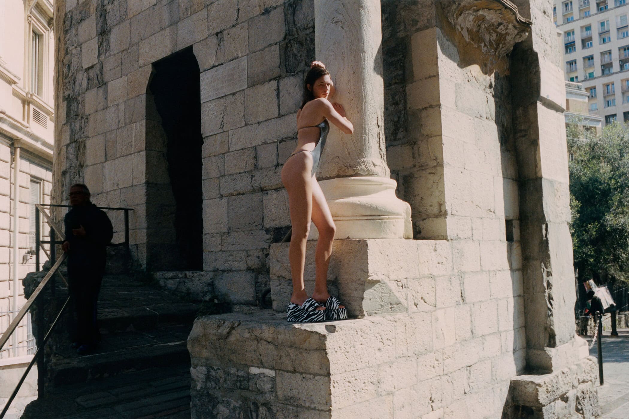 Adele Aldighieri in a metallic swimsuit and zebra-print platform sandals poses on ancient stone ruins for The Attico.