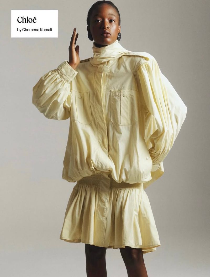 Model Kethia Ngeleza wearing a voluminous pale yellow high-neck jacket and pleated mini skirt against a light studio backdrop.