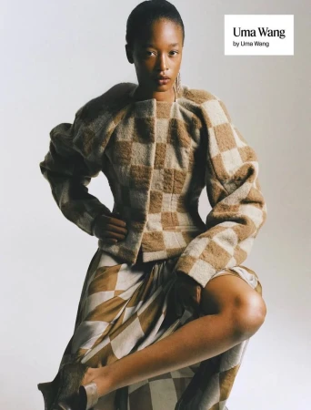 Model Kethia Ngeleza posing in a checkered structured jacket and patterned skirt against a neutral studio backdrop.