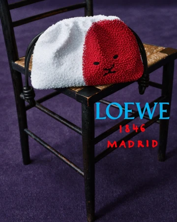 A red and white beaded drawstring pouch bag with a minimalist face resting on a black wooden chair over a purple carpet.