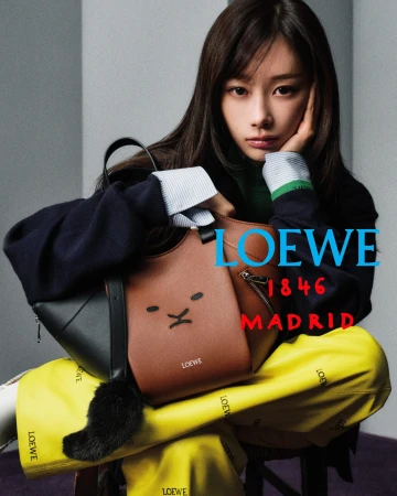 Giselle seated in yellow Loewe trousers holding a brown and black leather Loewe handbag for an advertising campaign.