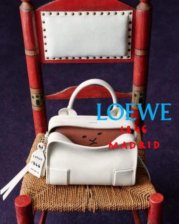 White leather Loewe handbag resting on a rustic red painted chair with woven rush seat on a purple floor.