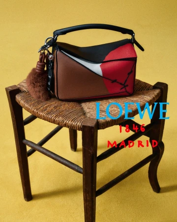 Loewe colorblocked leather handbag with a plush charm sitting on a rustic woven wooden chair against a yellow background.
