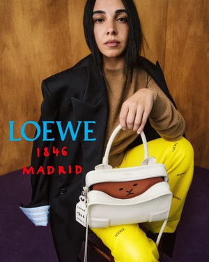 Salma Abu Deif posing with a white Loewe leather handbag while wearing yellow branded trousers and a draped black blazer.