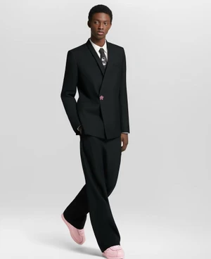 A Black man wearing a black suit and pink sneakers posing against a seamless white background.