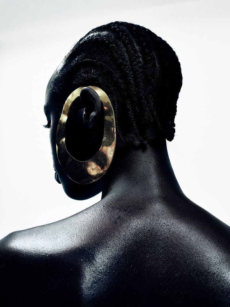 Back view of a Black model with braided hair wearing an oversized sculptural gold earring against a white background.
