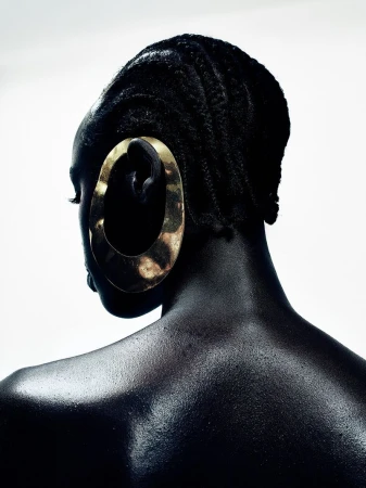 Back view of a Black model with braided hair wearing an oversized sculptural gold earring against a white background.