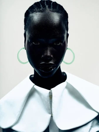 Close-up portrait of model Grace Ayup wearing circular mint hoop earrings and an oversized white collar against a light studio backdrop.