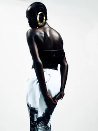Model Grace Ayup facing away in a black bandeau top, printed skirt, and large sculptural gold earring against a white studio background.