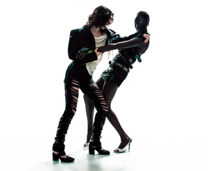 Two fashion models in distressed black garments and silver heels posing dynamically against a bright white background.