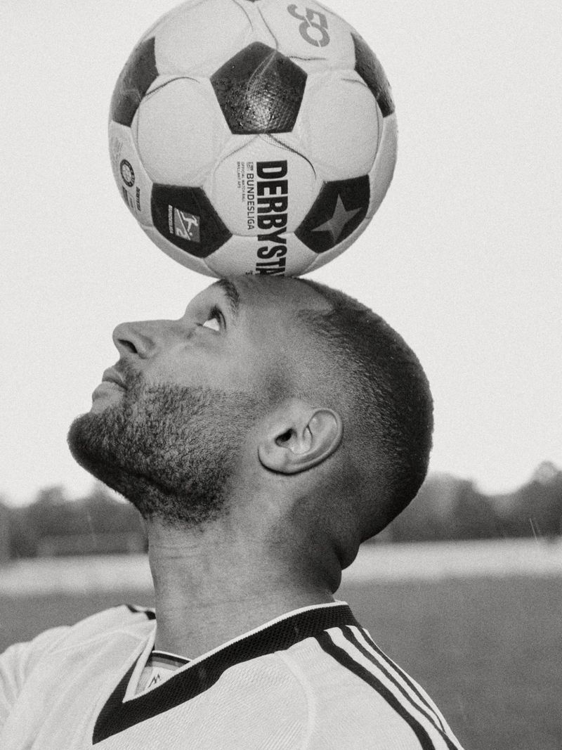 Jonathan Tah balances a classic soccer ball on his forehead in a black and white close-up profile shot.