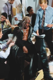 Group of diverse office workers surrounding a shirtless man with braided blonde hair wearing high leather boots