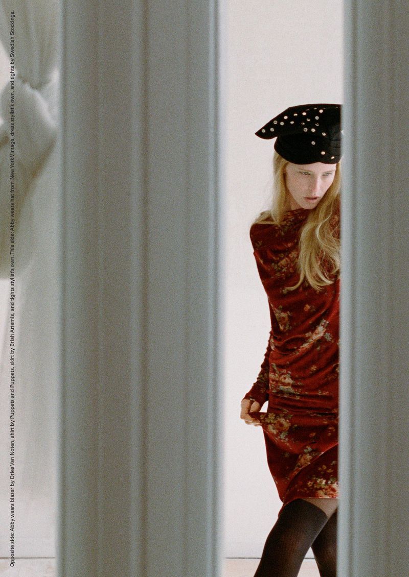 A woman in a patterned velvet dress and beret stands in front of white columns, partially obscured from view. Fashion editorial photography.