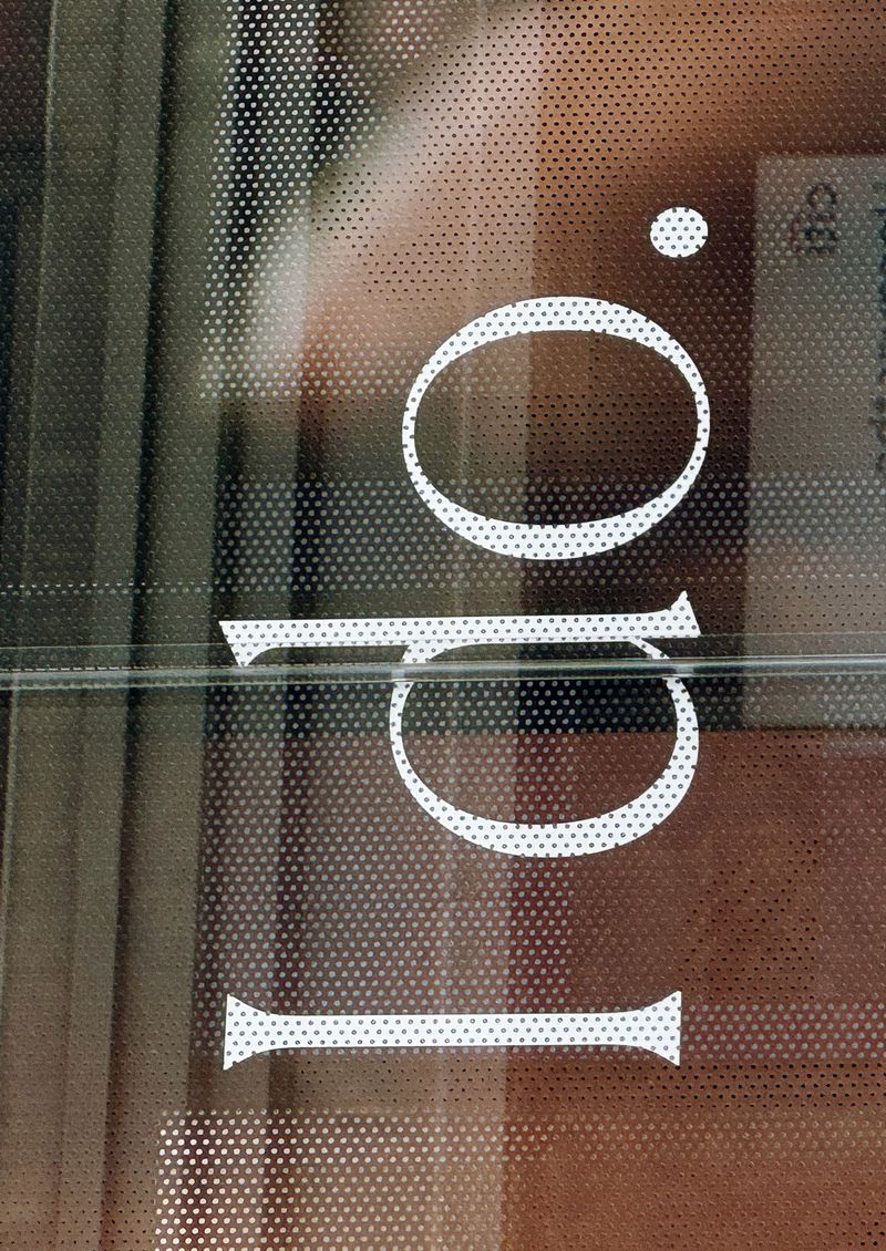 Close-up of a perforated film on glass with a white text overlay, featuring large numbers and letters on a reflective surface.