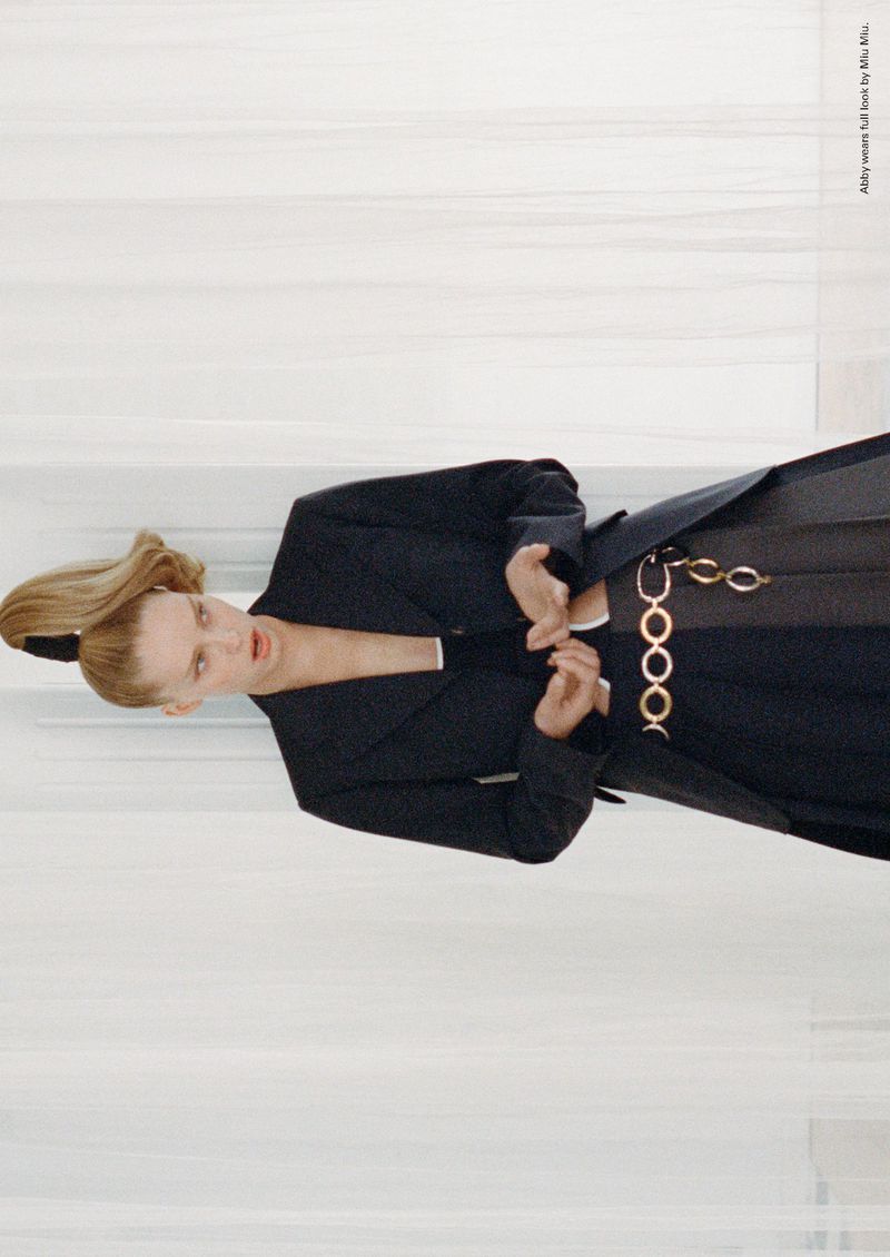 Model Abby Champion wearing a dark blazer and chained belt against a pale curtain backdrop for ALL-IN 08 editorial