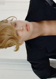 Model Abby Champion posing in an open black blazer with styled wave blonde hair against a neutral backdrop.