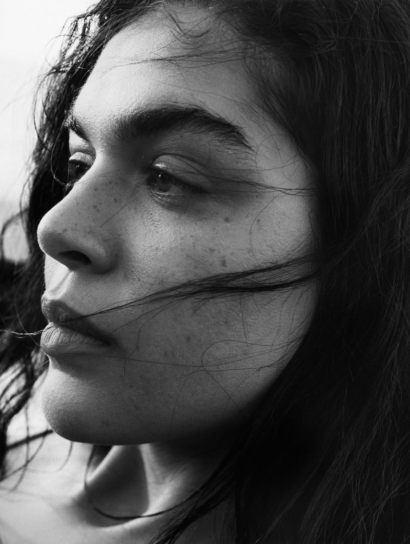 Monochrome portrait of a young adult female with dark hair and freckles, close-up profile view against a light background.