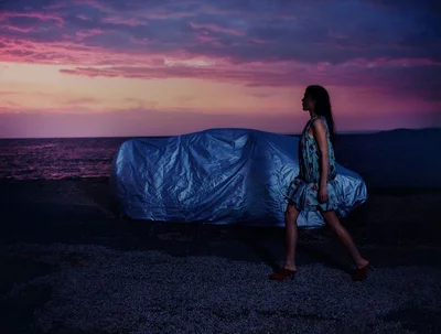 Model walking past a covered car on a shoreline at sunset for Elle Sweden Marseille