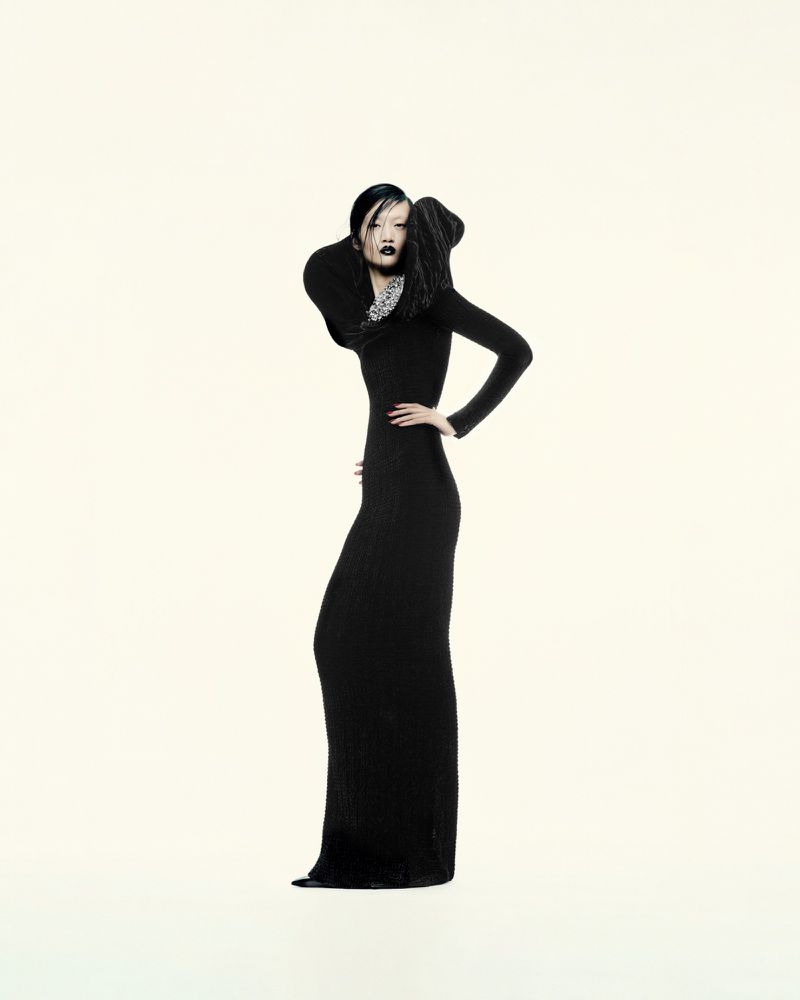 Model Yilan Hua posing in a floor-length sculptural black gown with a high dramatic collar against a pale studio backdrop.