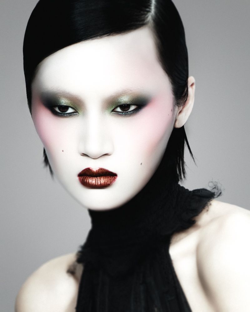 Close-up beauty portrait of model Yilan Hua featuring smoky green eye makeup, metallic dark lips, and a high black ruffled collar.