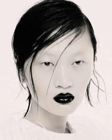 Close-up beauty portrait of model Yilan Hua with slicked wet hair and glossy black lipstick against a white seamless background.