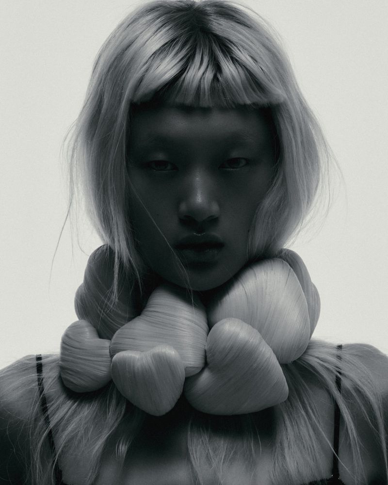 Model Yilan Hua wearing an avant-garde collar of heart-shaped blonde hair forms against a light studio backdrop.
