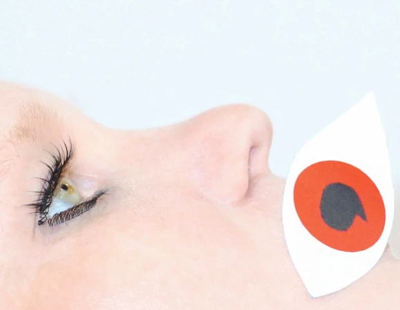 Extreme close-up profile of a person with a paper cutout eye placed over their mouth against a white background.