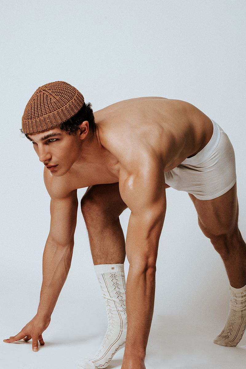 Athletic man in a crouched position, wearing a knit cap and socks, captured in a studio setting with a clean white background.