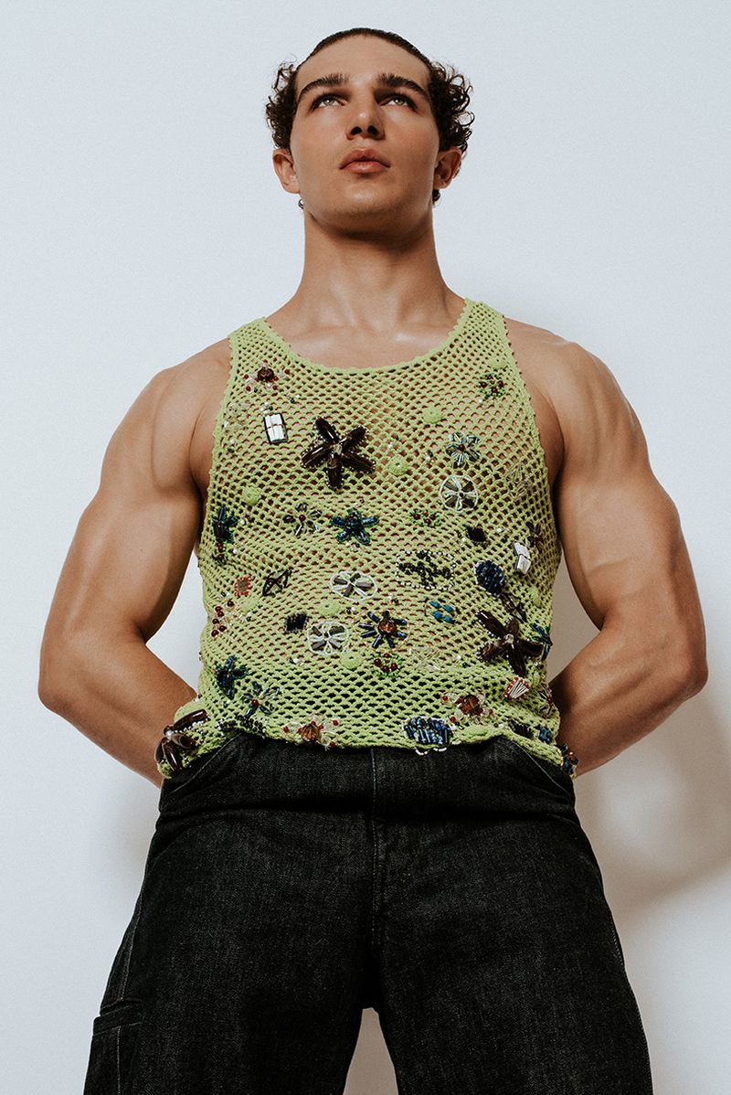Model Sacha Bilal wearing an embellished lime green crochet tank top and black jeans against a white seamless background.