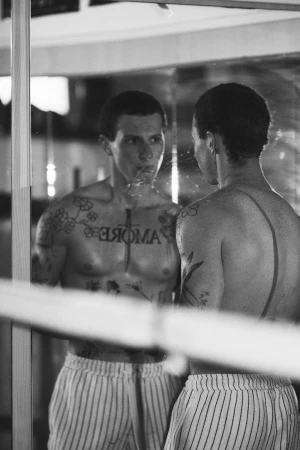 Black and white reflection of a shirtless tattooed man looking into a mirror wearing striped shorts.