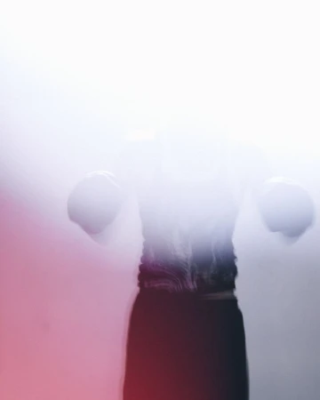 Motion-blurred silhouette of a figure in boxing gloves enveloped by high-key white light and soft red peripheral glow.