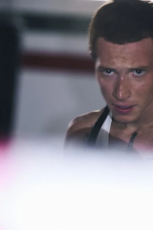 Close-up portrait of an athletic man in a white tank top with an intense gaze against a soft blurred background.