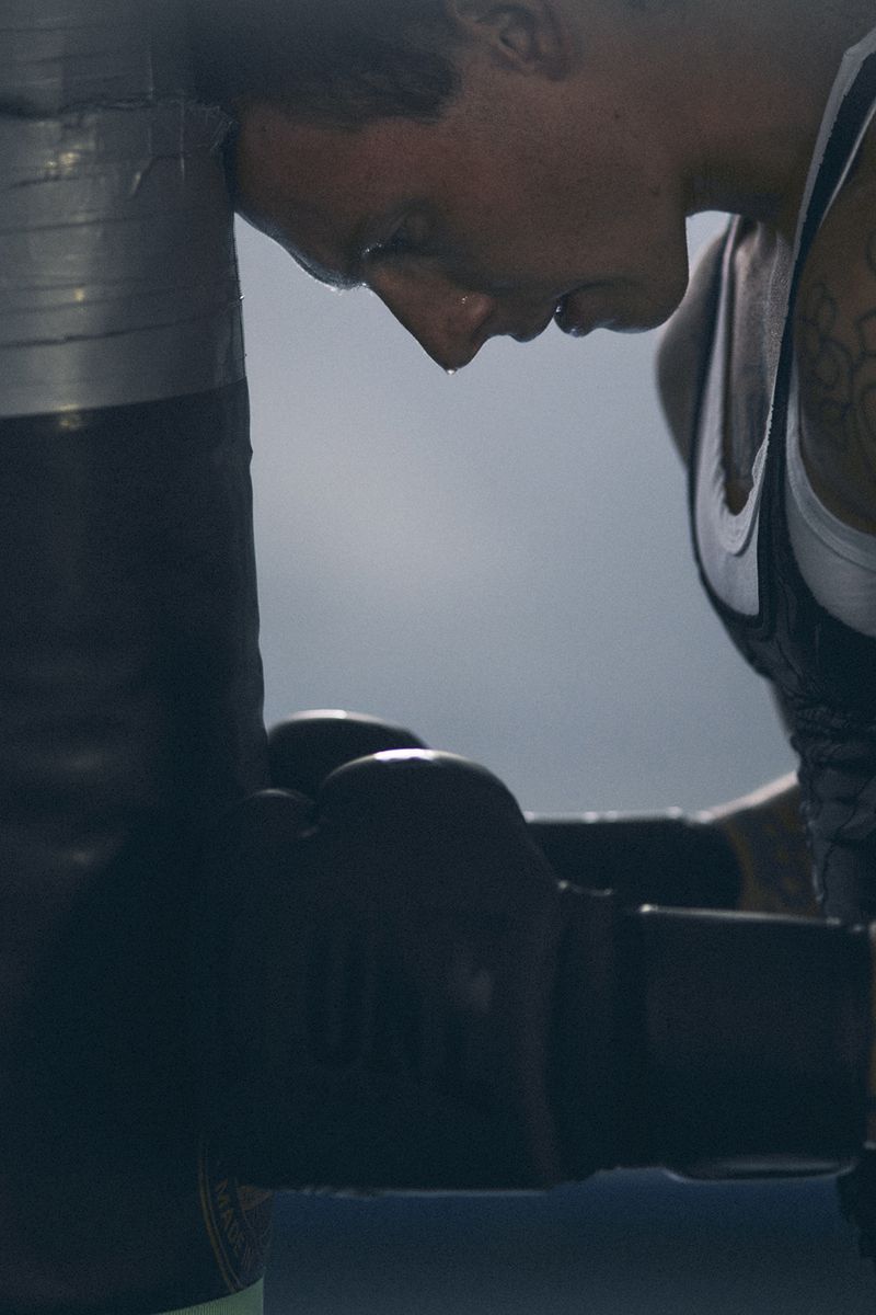 Exhausted boxer leaning forehead against a heavy bag wearing boxing gloves in a gym for CRUSHfanzine