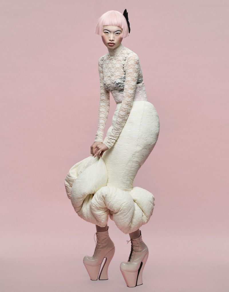 Model Chun Jin in a sheer lace top, sculptural padded bubble skirt, and heel-less boots against a solid pink backdrop.