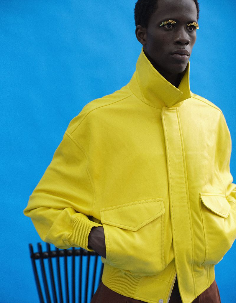 Model wearing a bright yellow high-collar jacket against a vivid blue background for an Esquire China editorial shoot.
