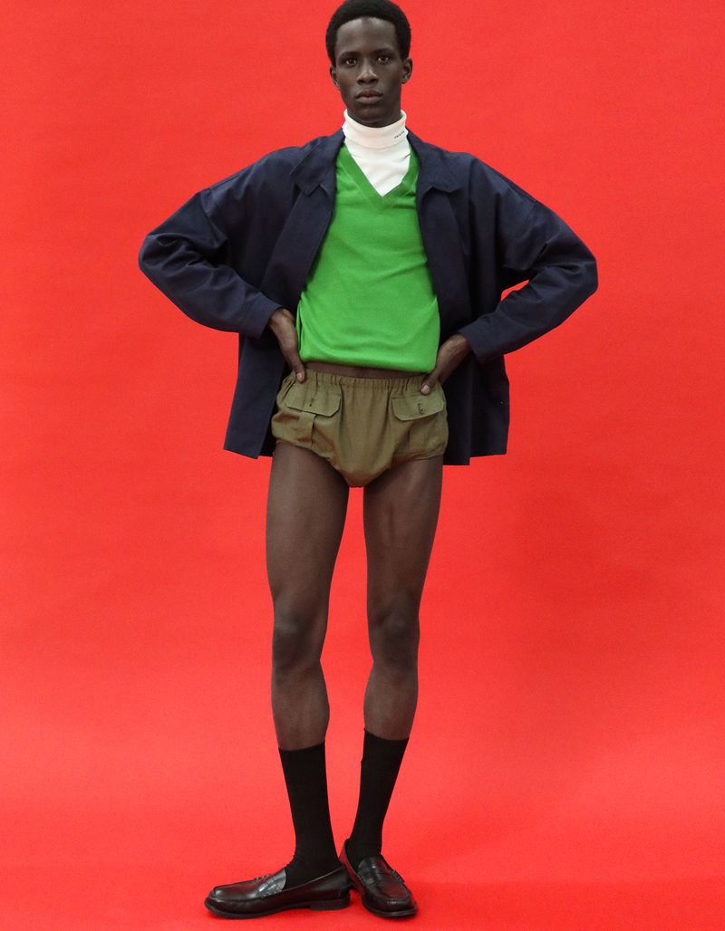 Khalil Bayo wearing a green v-neck, navy jacket, and khaki shorts against a vibrant red backdrop for Esquire China.
