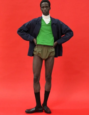 Khalil Bayo wearing a green v-neck, navy jacket, and khaki shorts against a vibrant red backdrop for Esquire China.