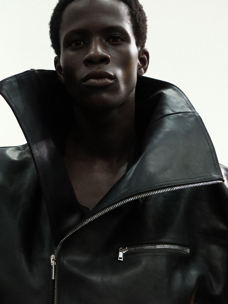 Model Khalil Bayo wearing an oversized black leather jacket with an exaggerated high collar against a white background.